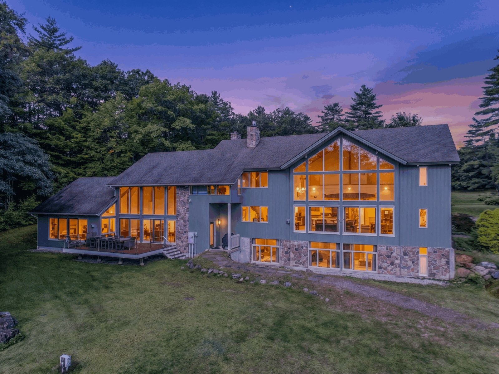 A large home with walls of glass, lit from inside at dusk
